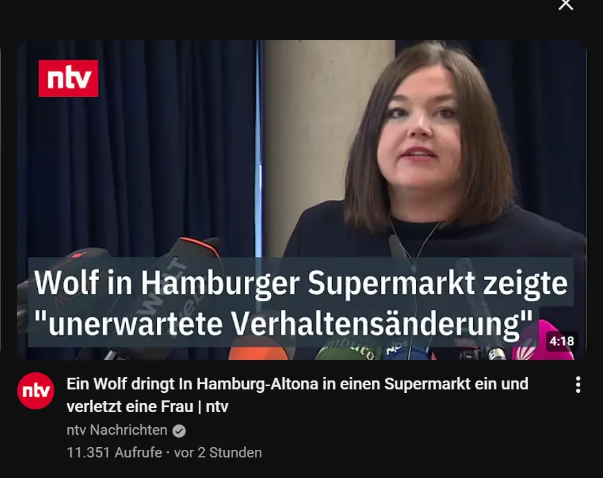 Eine selbstbewusste Frau in einem dunklen Blazer spricht auf einem blau beleuchteten Podium zu den Zuh&ouml;rern; daneben steht ein deutscher Text, in dem von einem seltsamen Auftritt eines Wolfs in Hamburg die Rede ist.
